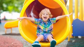 Boy with blonde hair coming out of yellow tube slide