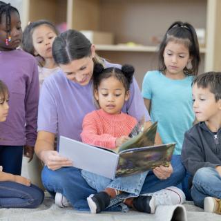Group of children reading a book with a teacher