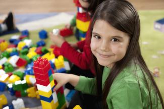 little girl smiling while playing with duplos
